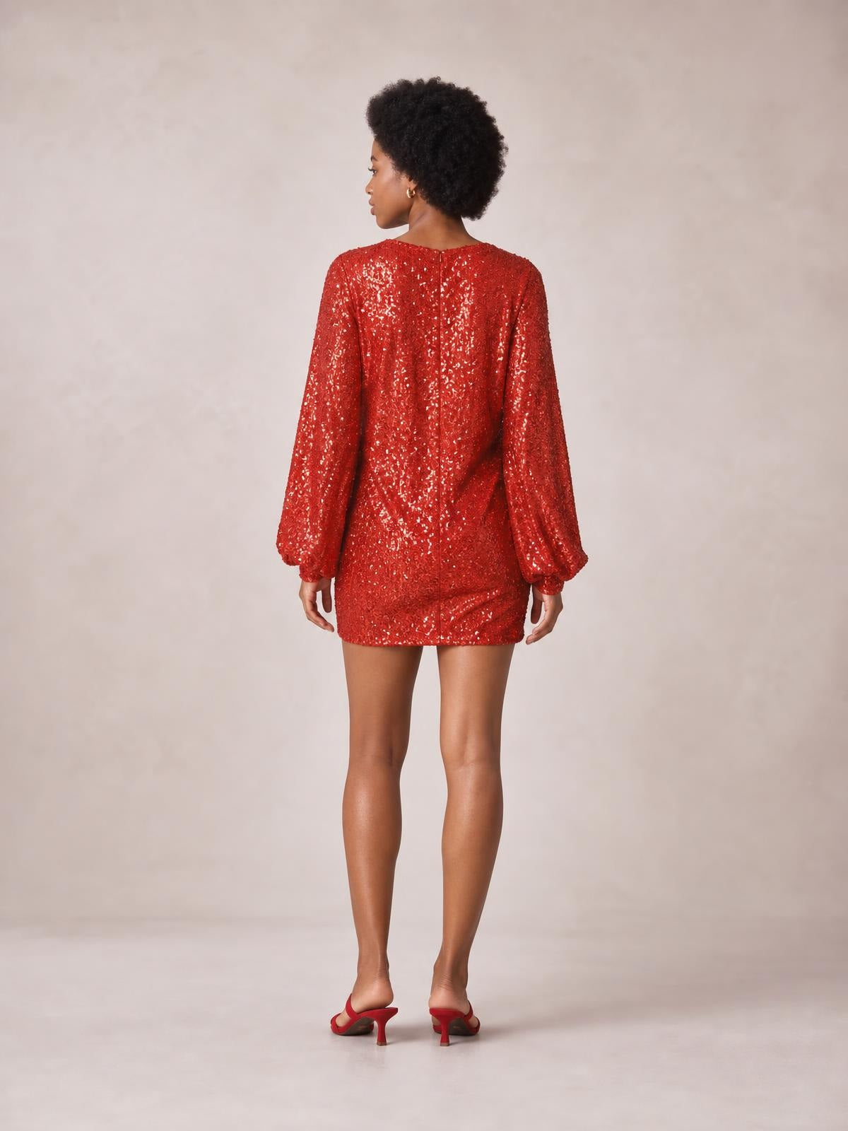 Model shown from the back in a red sequin mini dress with long sleeves, gathered cuffs, a straight silhouette, and visible center-back closure.