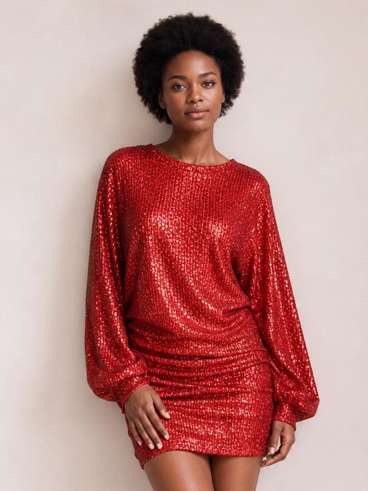 Model wears a red sequin long sleeve mini dress with a round neckline, relaxed silhouette, and ruched detailing through the waist and skirt.