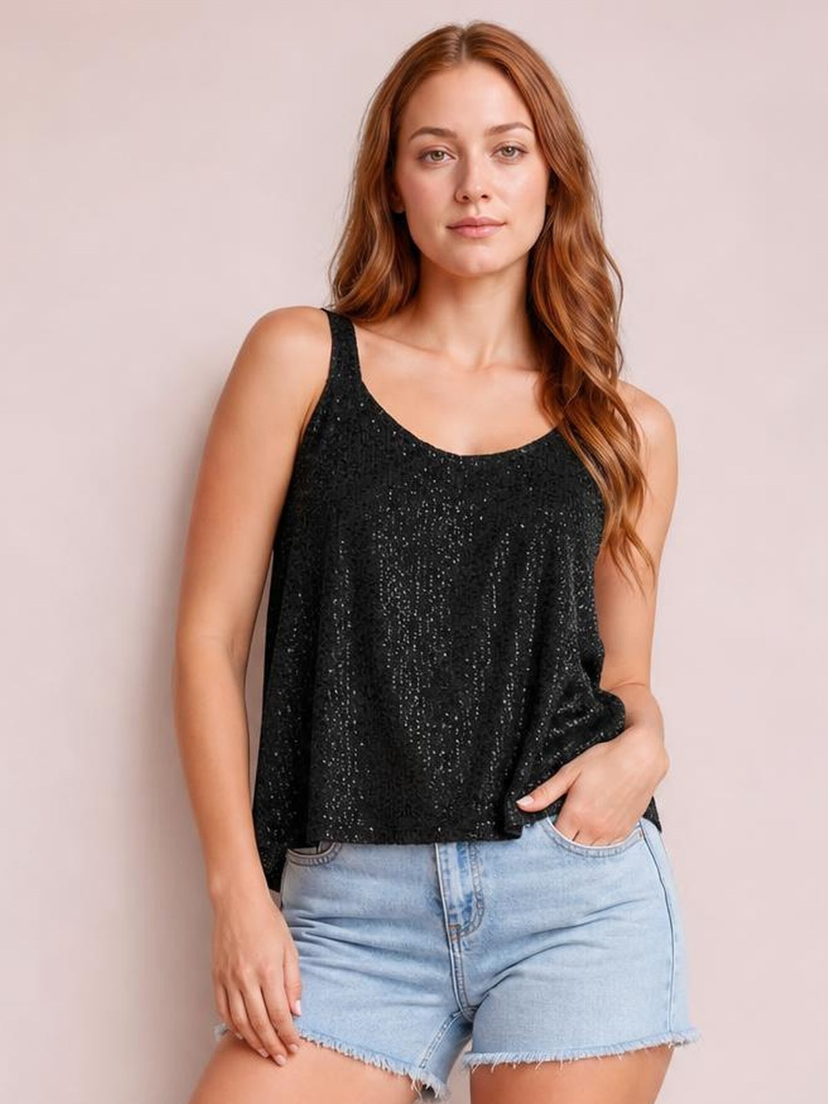 Model wears a black sequin scoop neck tank with wide shoulder straps and a relaxed straight silhouette, posing with one hand in her denim shorts pocket.