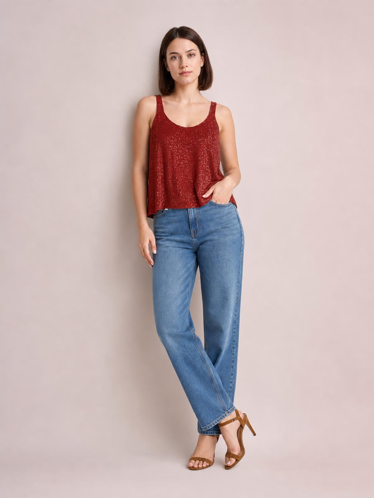 Model poses in a red sequin scoop neck tank with wide shoulder straps and a relaxed straight silhouette, paired with blue jeans.