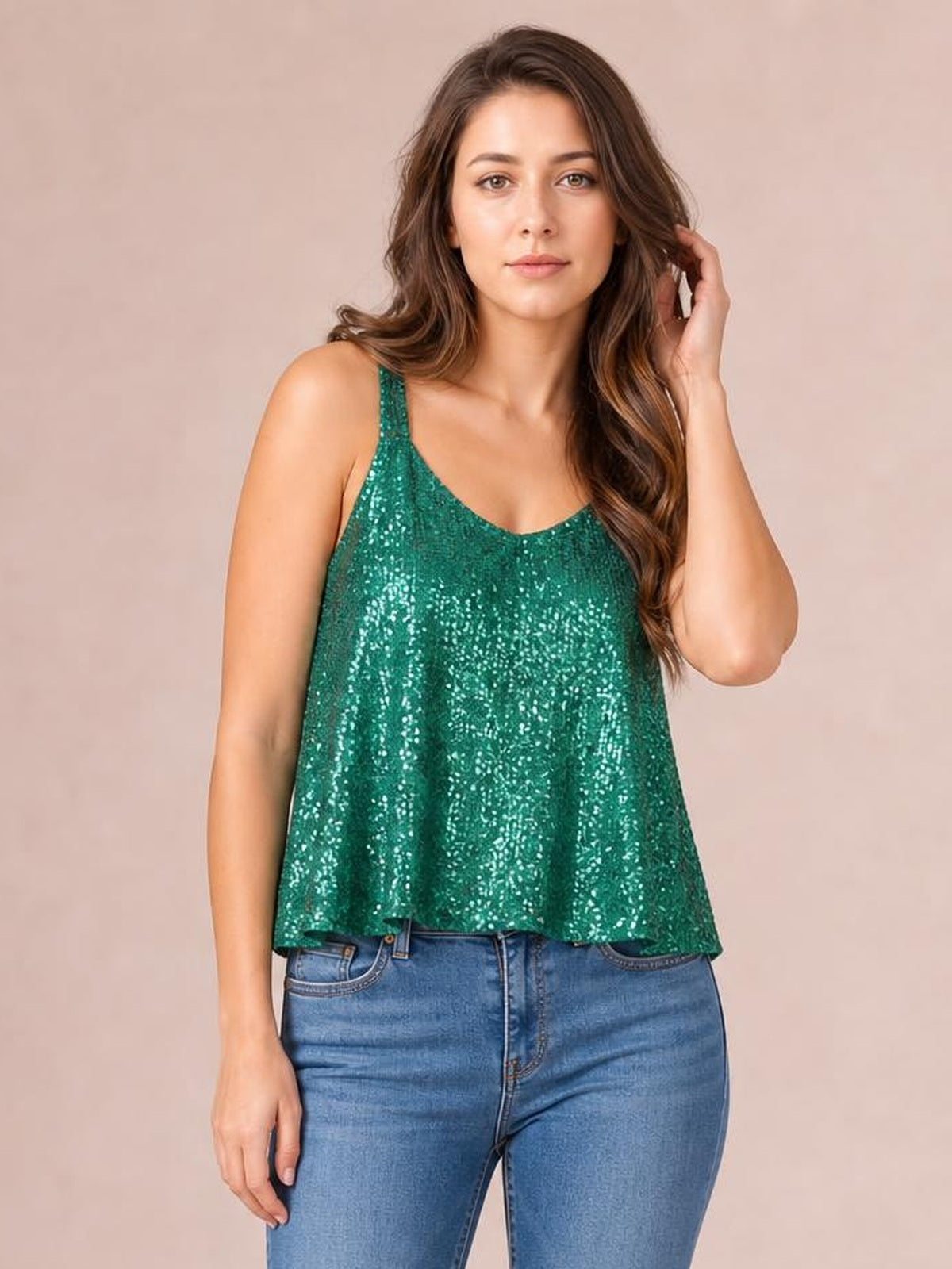 Model wearing a green sequin scoop neck tank with slim straps and a relaxed, slightly flared silhouette, posed with one hand touching her hair.