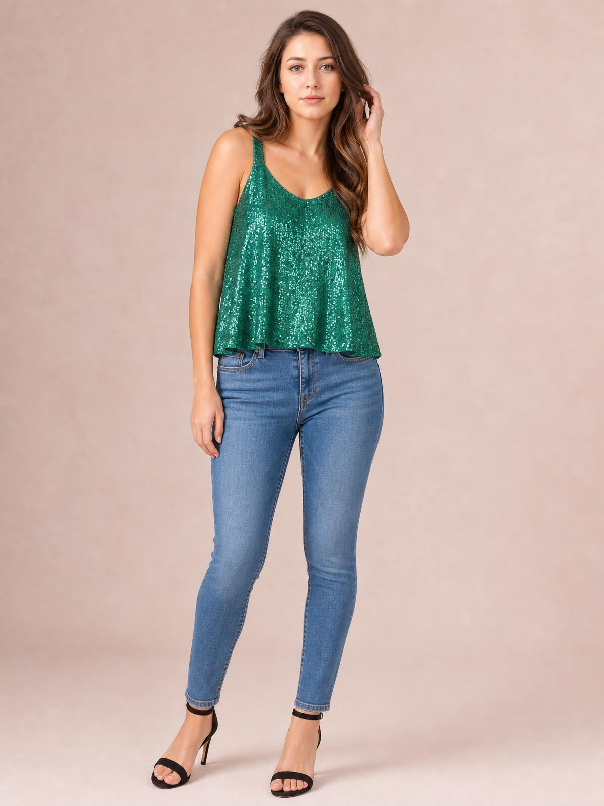 A model stands in a shimmering emerald sequin scoop neck tank with wide straps and a relaxed, flowing silhouette, lightly touching her hair.