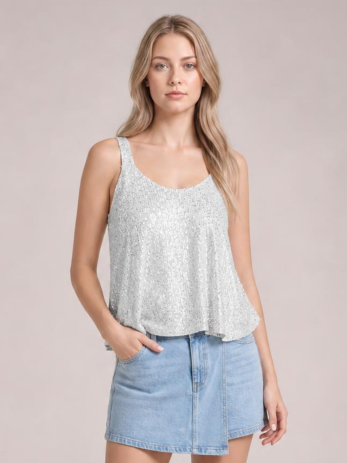 A model wears a shimmering silver sequin scoop neck tank with wide straps and a relaxed, slightly flared silhouette, posing with one hand in her pocket.