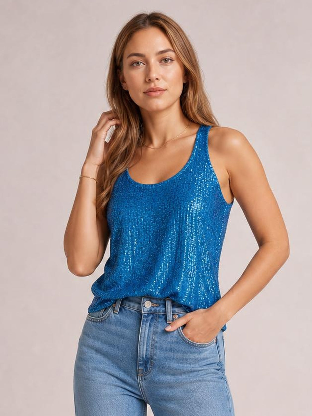 Model poses in a bright blue sequin scoop neck tank with wide shoulder straps and a relaxed silhouette, one hand in her jeans pocket.