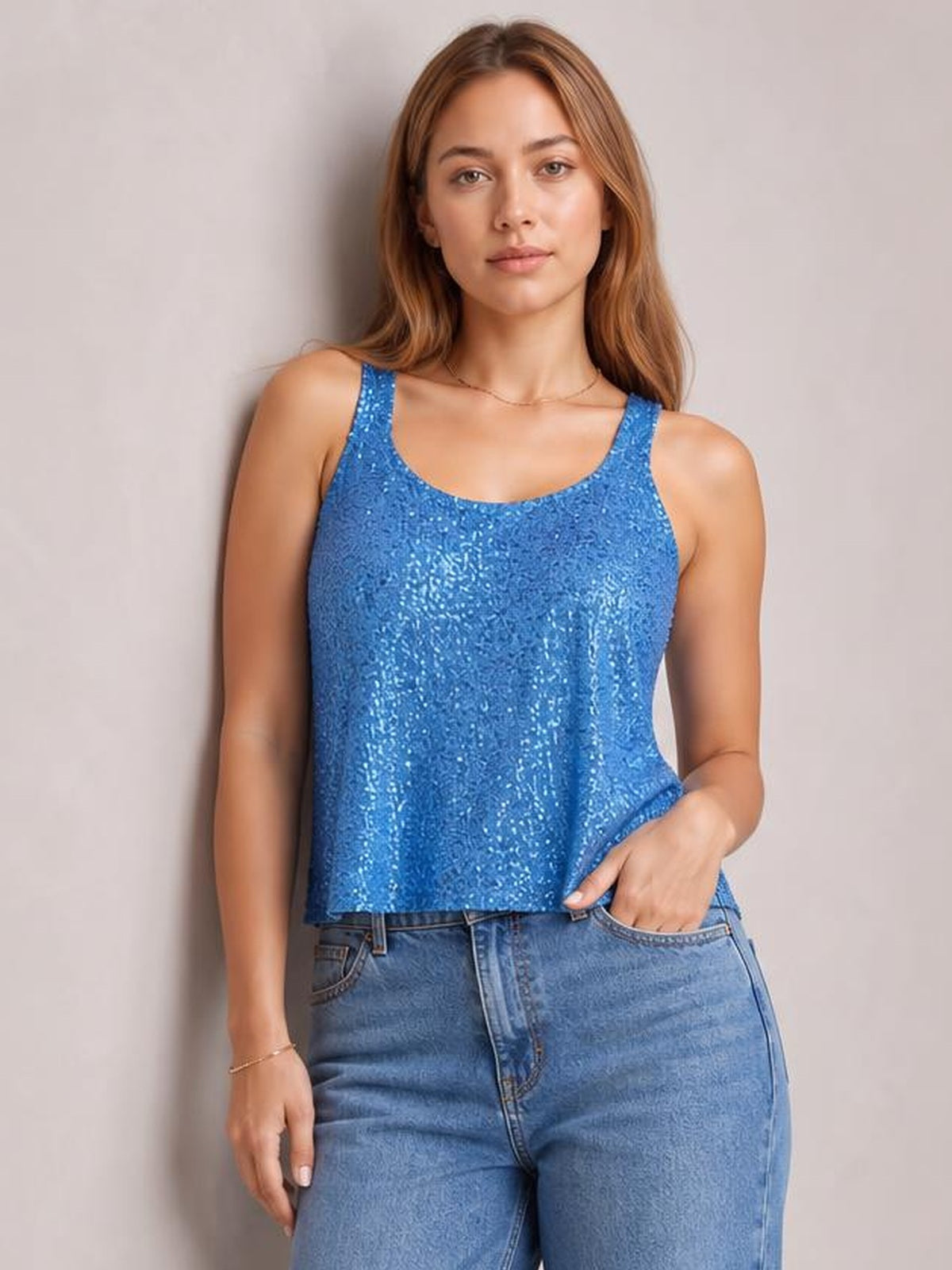 Model wears a blue sequin scoop neck tank with wide shoulder straps and a relaxed straight silhouette, posing with one hand in her jeans pocket.