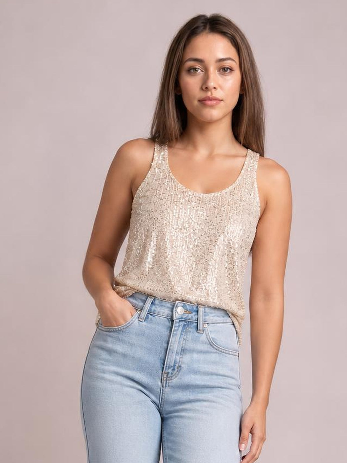 A model poses with one hand in her pocket wearing a champagne sequin scoop neck tank with wide shoulder straps and a relaxed, slightly sheer-looking silhouette.