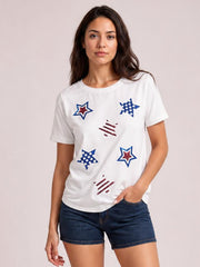 Model poses with one hand in her pocket wearing a white round-neck short-sleeve T-shirt with colorful sequin star motifs and a relaxed silhouette.