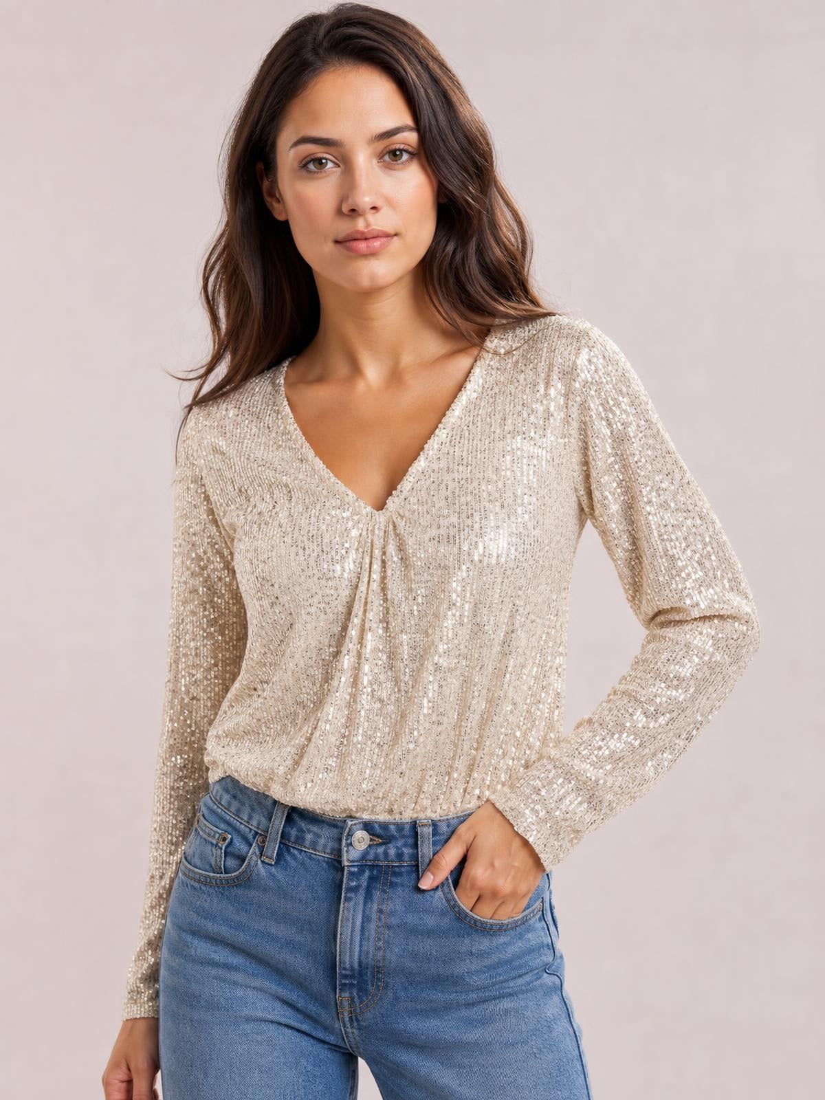 Model poses with one hand in her jeans pocket wearing an ivory sequin surplice long-sleeve bodysuit with a fitted silhouette and gathered wrap front.