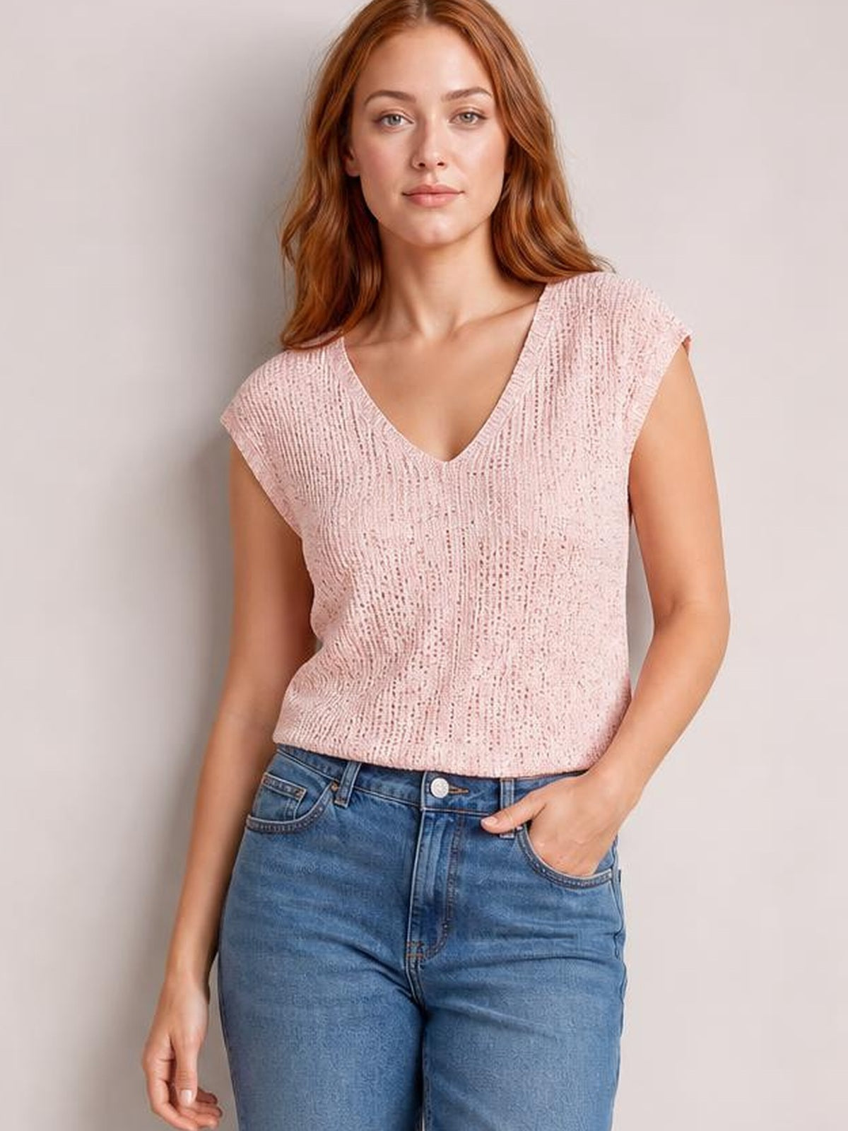 Model wearing a pale pink sequin V-neck cap sleeve top with a relaxed silhouette, tucked into jeans, posing with one hand in a pocket.
