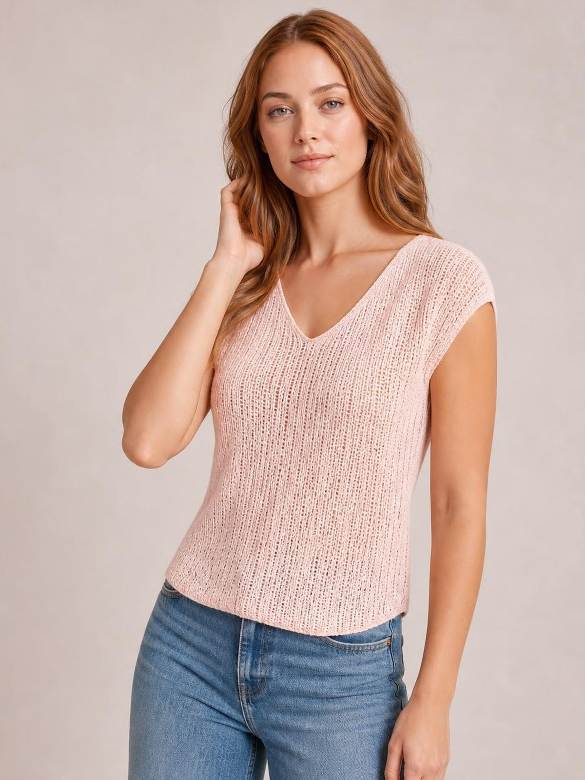 A model poses in a pale pink V-neck cap-sleeve top with a fitted straight silhouette and textured vertical construction, touching her hair.