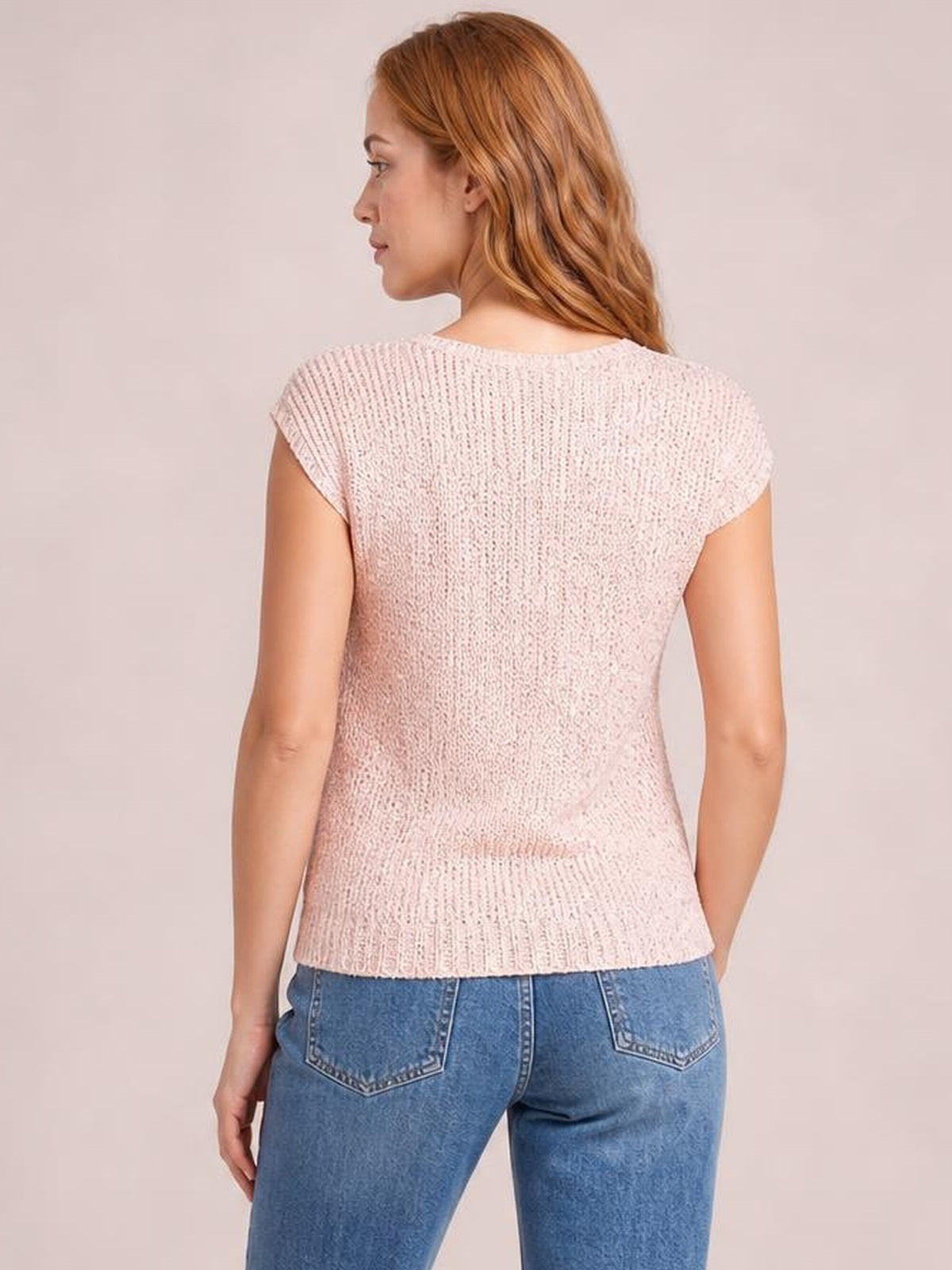 Back view of a model wearing a pale pink sequin cap sleeve top with a softly fitted silhouette, textured finish, and straight hem.