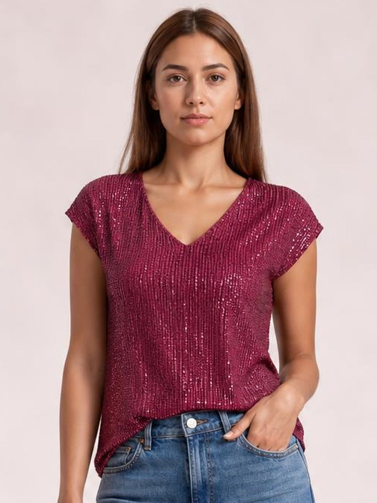 Model wearing a burgundy sequin V-neck cap sleeve top with a relaxed silhouette, opaque construction, and a straight hem over jeans.