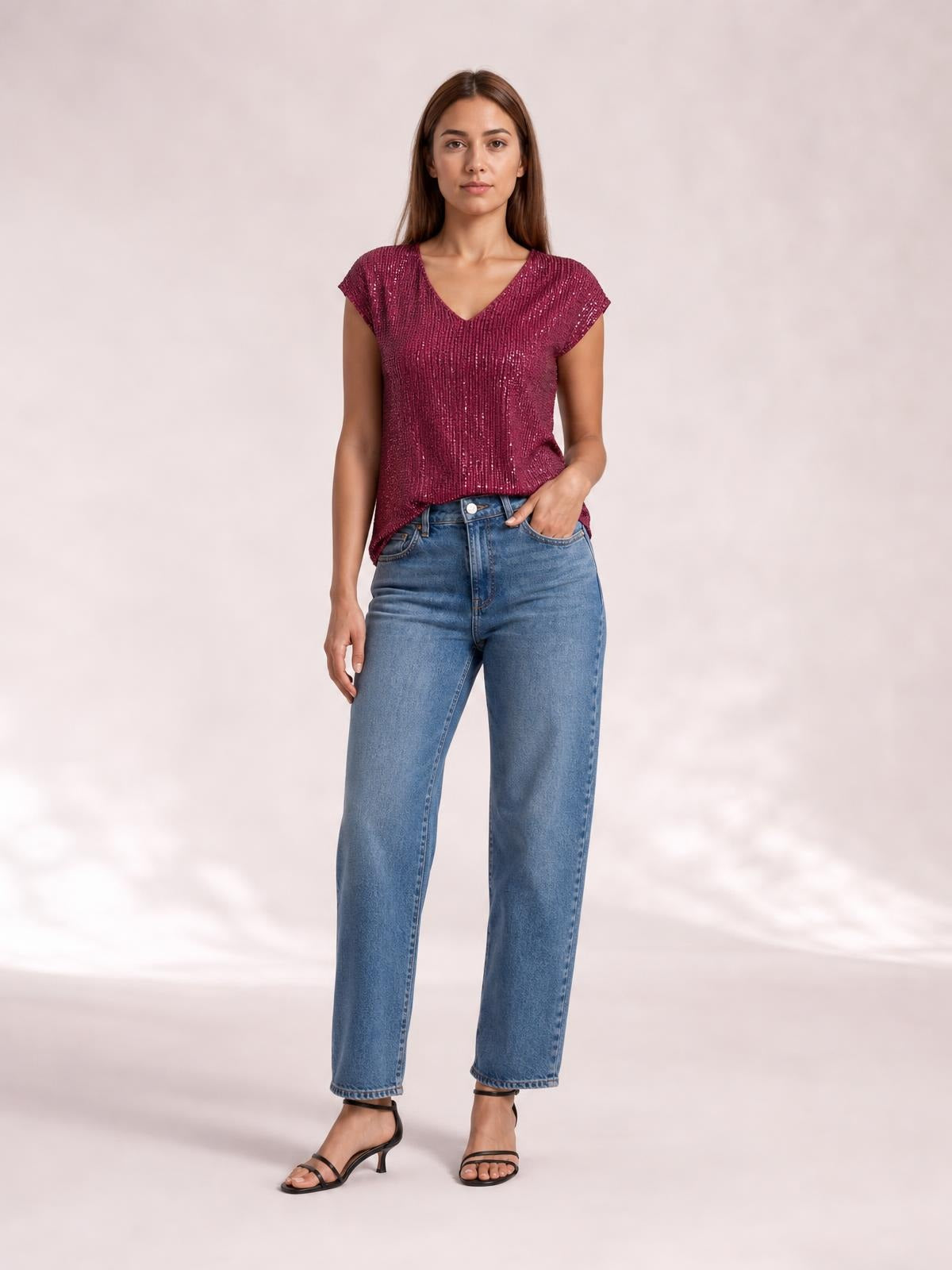 A model stands with one hand in her jeans pocket wearing a magenta sequin V-neck cap-sleeve top with a relaxed, straight silhouette.