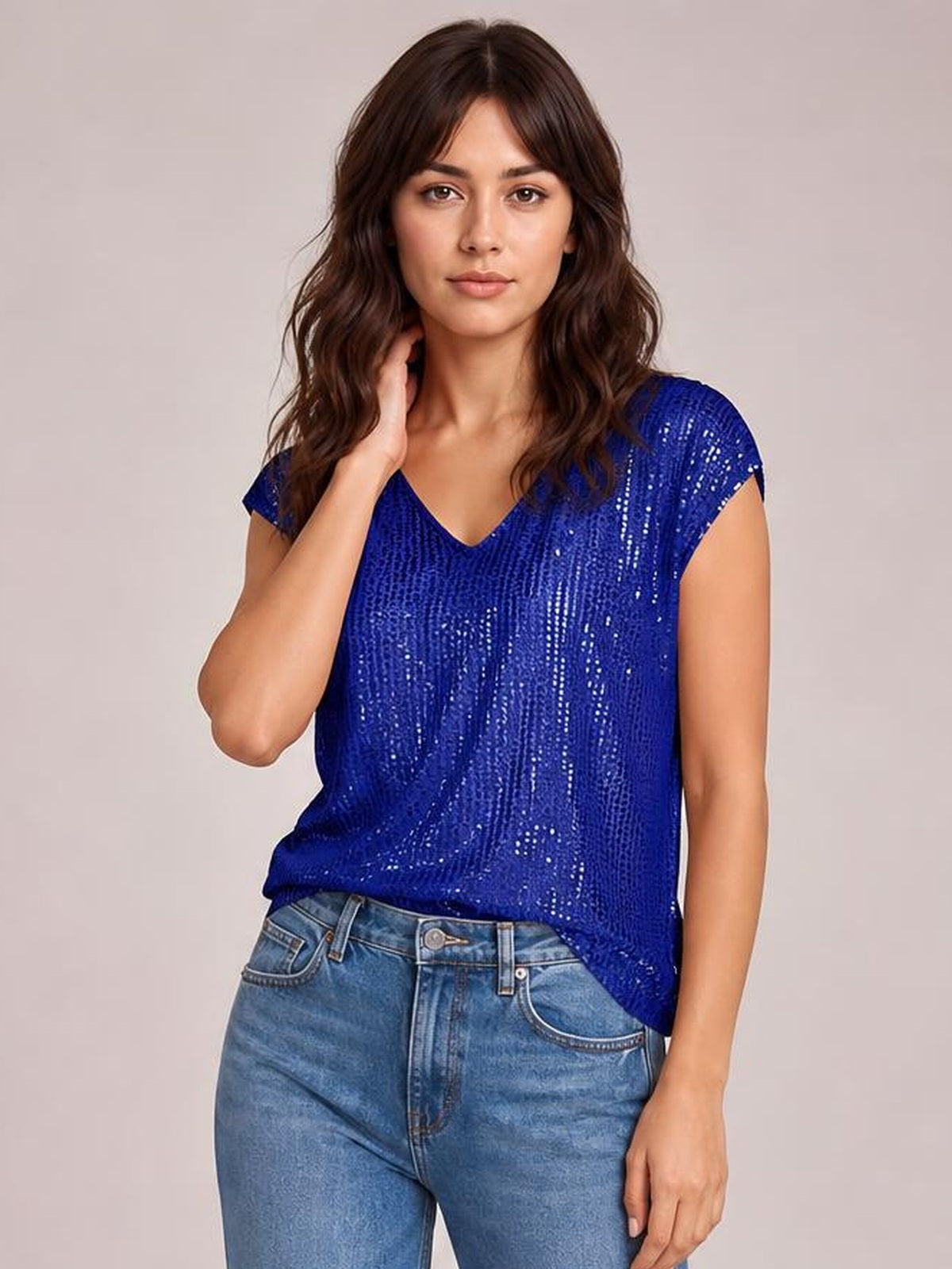 Model wearing a royal blue sequin V-neck top with cap sleeves, a relaxed straight silhouette, opaque construction, and sparkling vertical texture.
