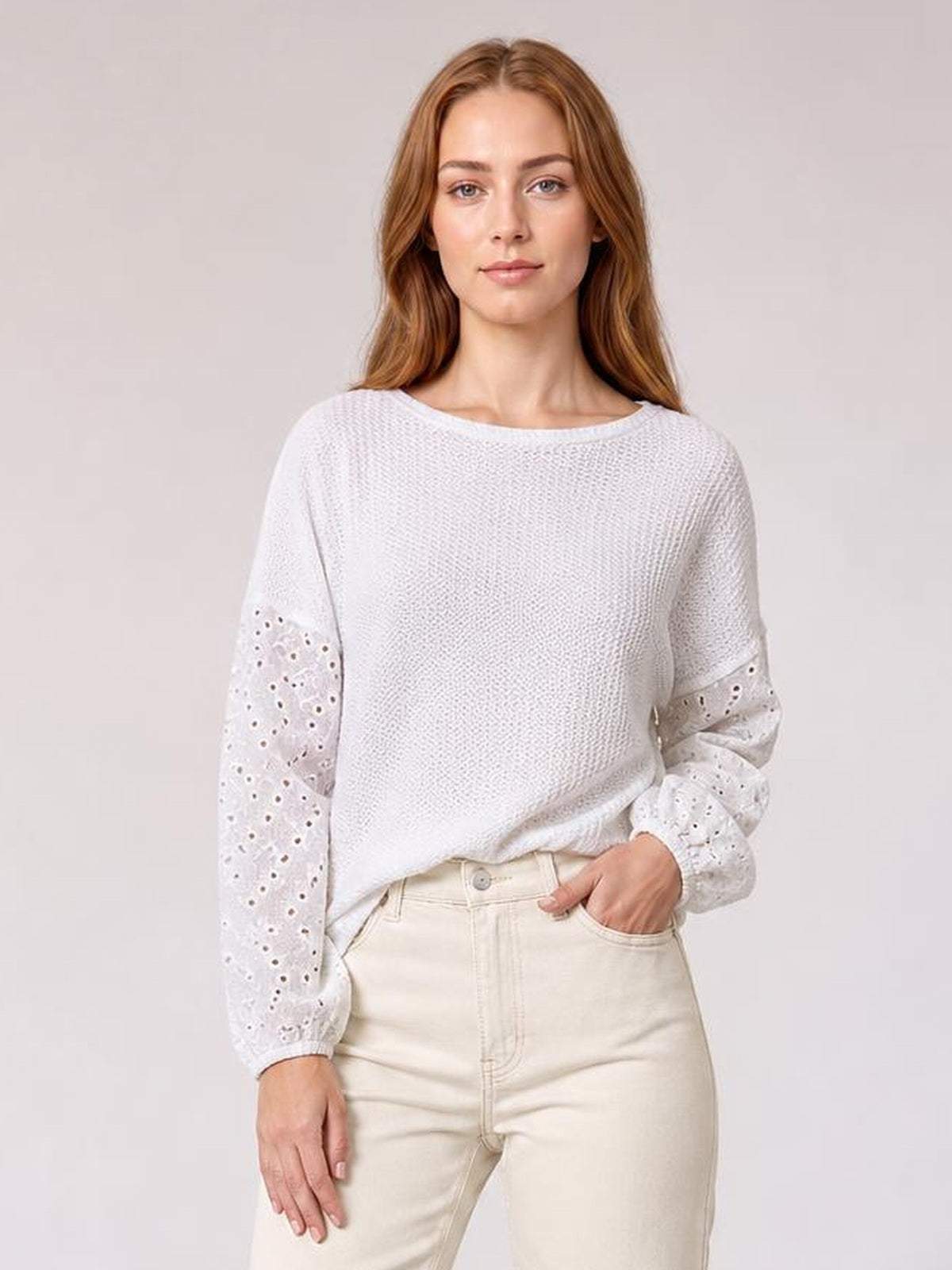Model wearing a white dropped shoulder round neck blouse with a relaxed silhouette and eyelet openwork sleeves, standing with one hand in her pocket.