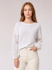 Model wearing a white dropped shoulder round neck blouse with a relaxed silhouette and eyelet openwork sleeves, standing with one hand in her pocket.