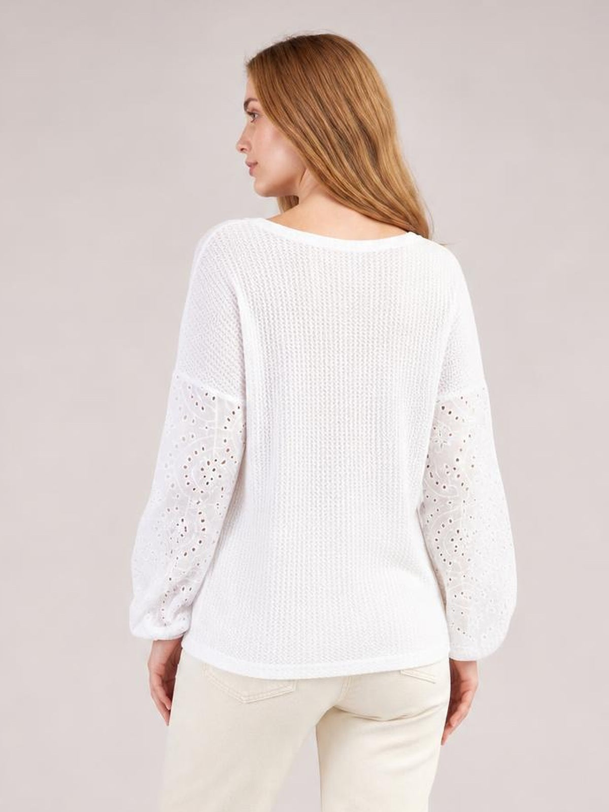 Model shown from behind in a white eyelet dropped shoulder blouse with a round neck, relaxed silhouette, textured body, and long openwork sleeves.