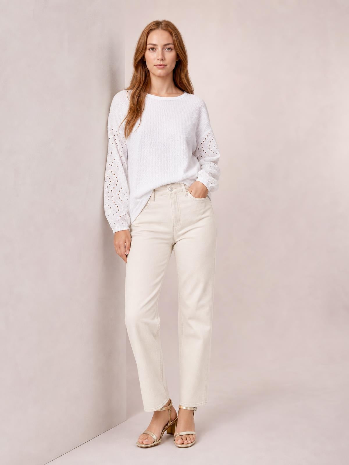 Model poses in a white round-neck blouse with dropped shoulders, relaxed silhouette, textured front, and eyelet openwork sleeves.