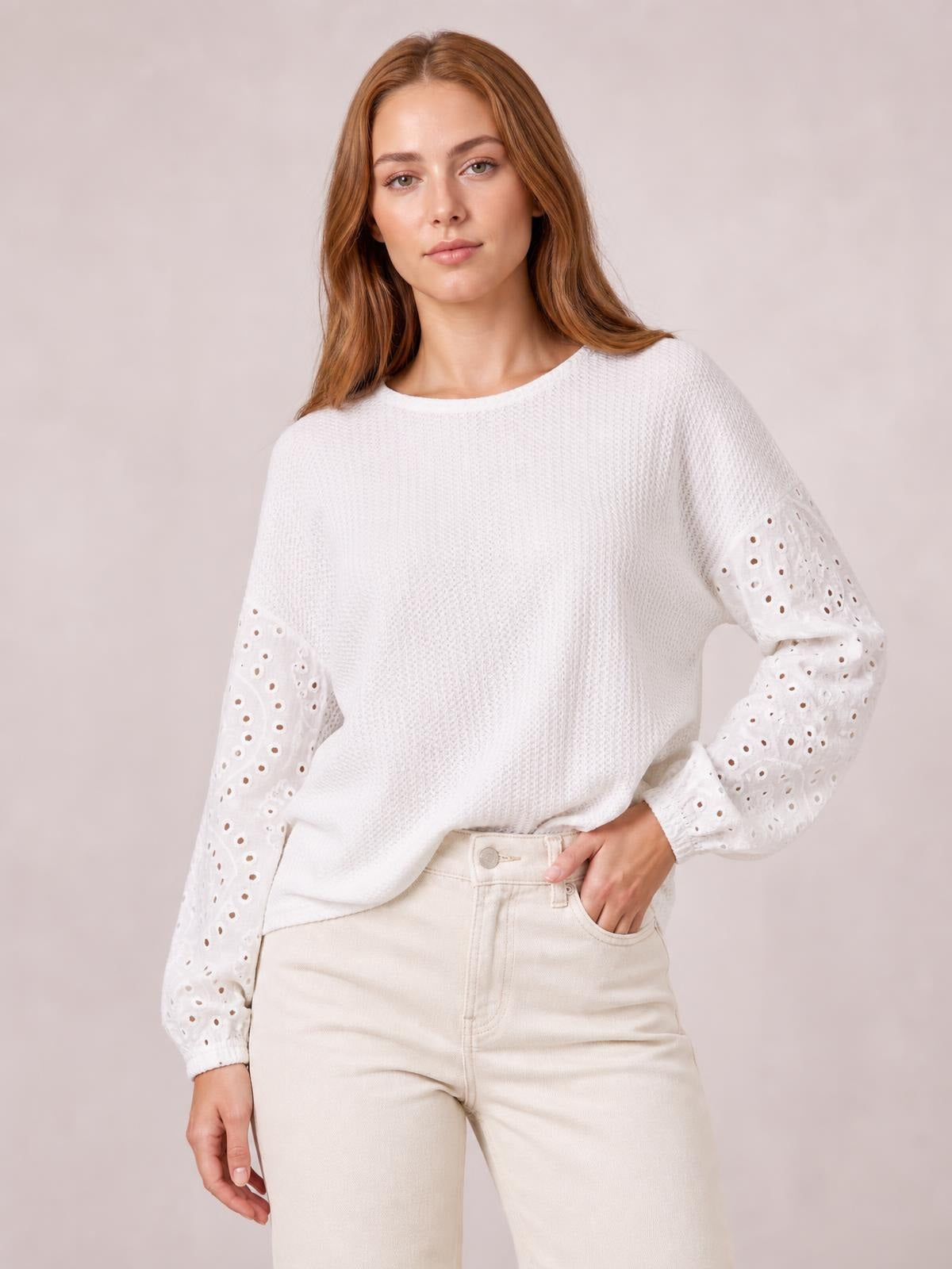 Model poses in a white dropped shoulder round neck blouse with textured fabric, relaxed silhouette, and eyelet openwork sleeves with elastic cuffs.