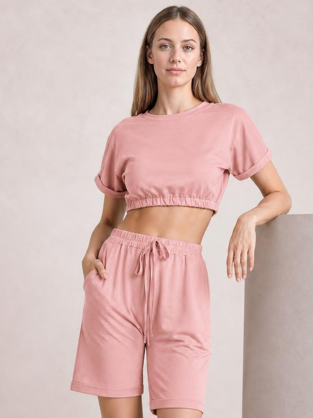 Model wearing a solid pink lounge set with a cropped short-sleeve round-neck top, rolled cuffs, elastic hem, and drawstring shorts.
