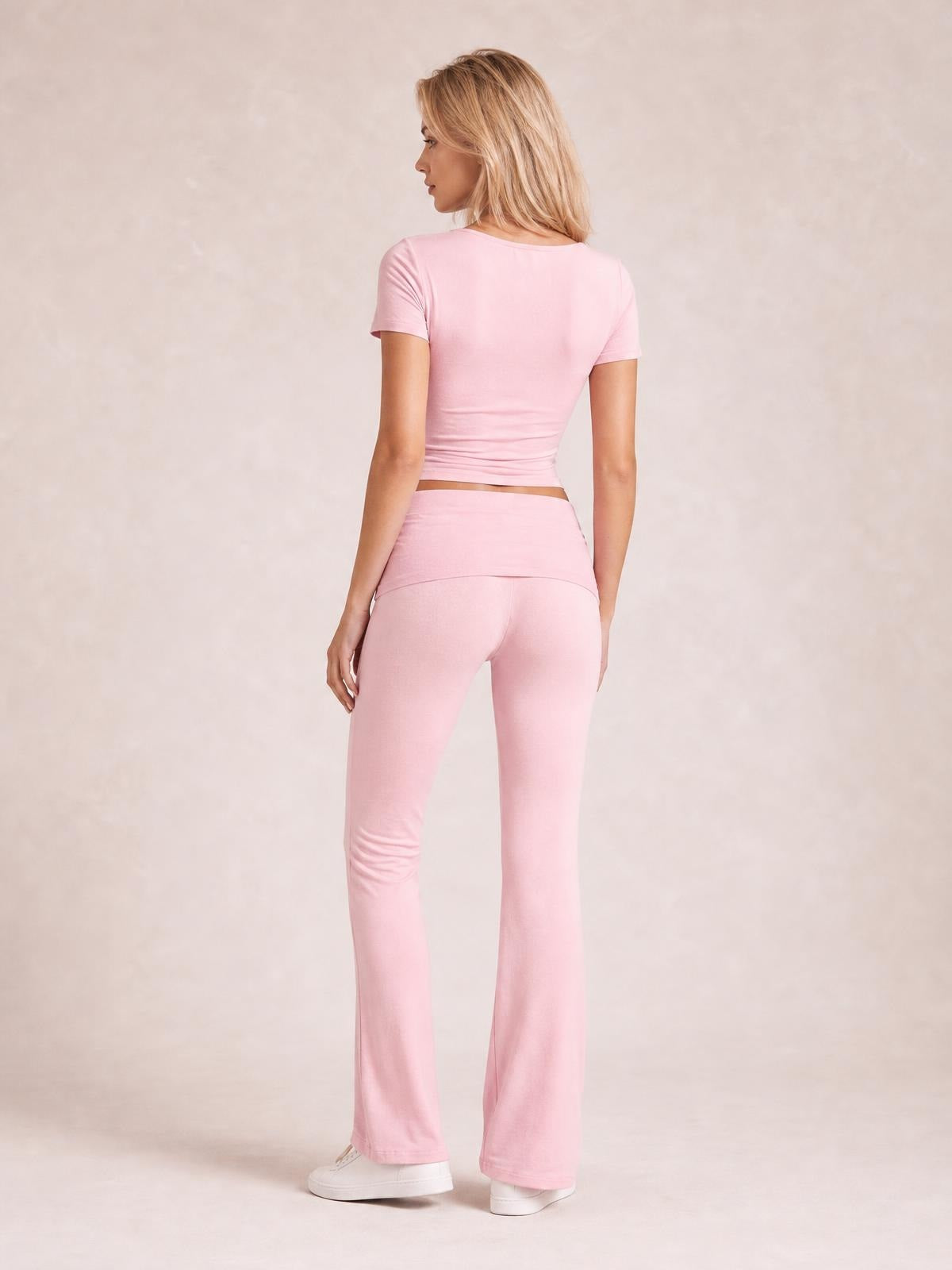 A model poses from the back in a pink short sleeve top and matching high-stretch bootcut leggings with a fitted silhouette and flared hems.