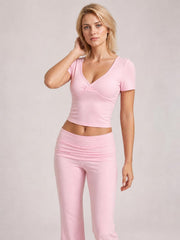 Model poses in a pink short sleeve top and matching bootcut legging set, featuring a fitted wrap-style neckline and ruched waistband.