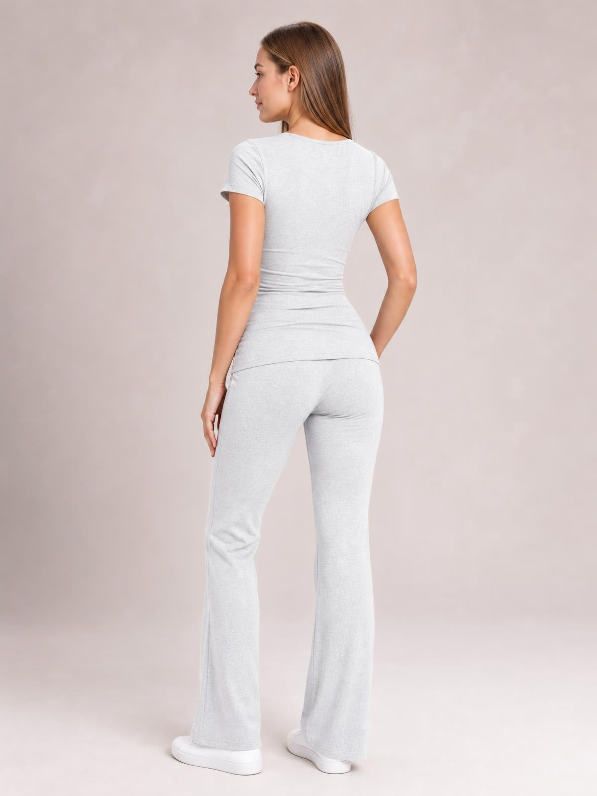 A model poses turned away in a light gray short sleeve top and matching bootcut legging set, showing the fitted silhouette and flared hems.