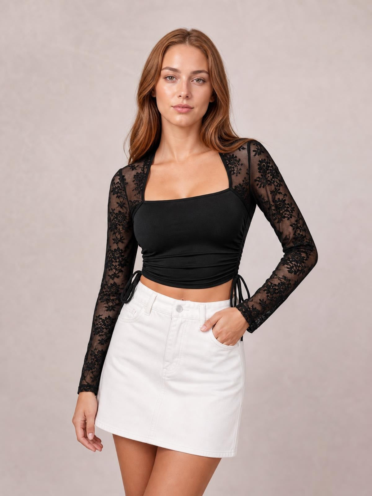 A model poses in a fitted black square-neck long-sleeve top with semi-sheer floral sleeves, side drawstrings, and a ruched cropped silhouette.