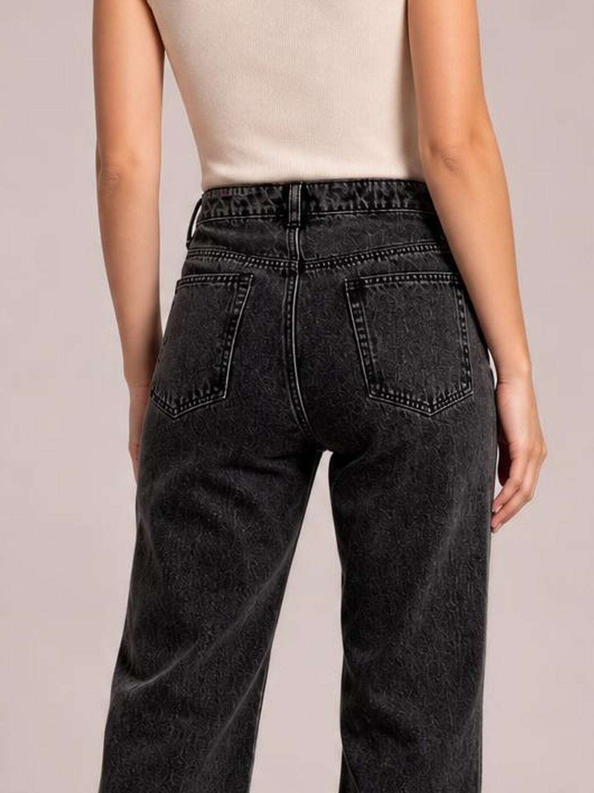 Model shown from behind wearing black high-waisted jeans with belt loops, contrast stitching, two back patch pockets, and a relaxed straight-leg silhouette.