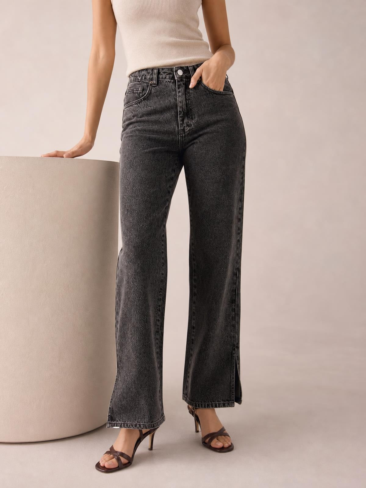 Model wearing charcoal side-slit jeans with front pockets, a buttoned waistband, and a straight wide-leg silhouette, standing in strappy heels.