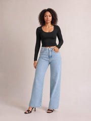 A model poses in light-wash wide-leg jeans with a high-rise waist, front pockets, button closure, and side slits at the hems.