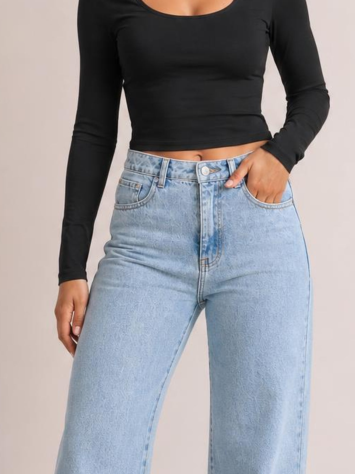 Model wears light-wash jeans with a high waist, belt loops, zip fly, front pockets, and a relaxed straight-leg silhouette, posing with one hand in a pocket.