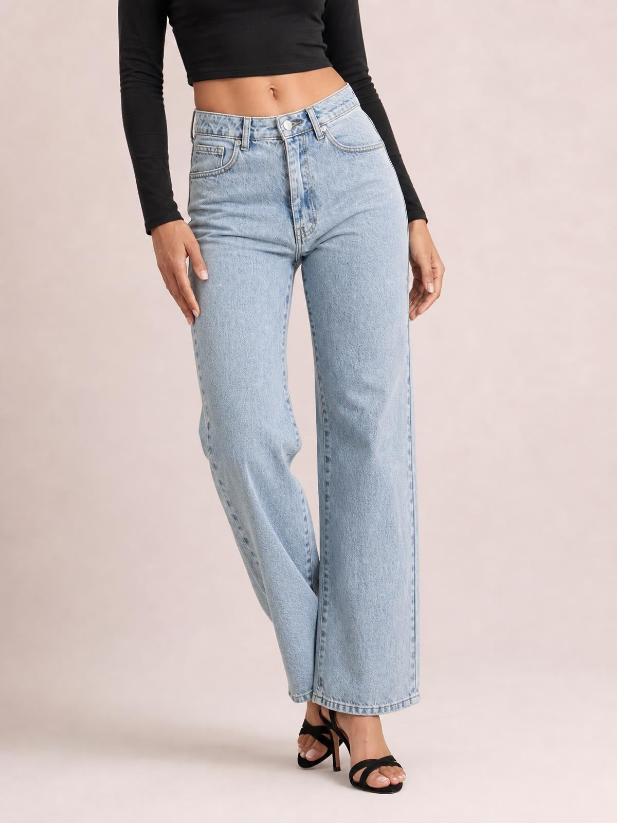 Model wears light-wash high-rise side slit jeans with front pockets, belt loops, button closure, and a relaxed wide-leg silhouette while crossing one leg.