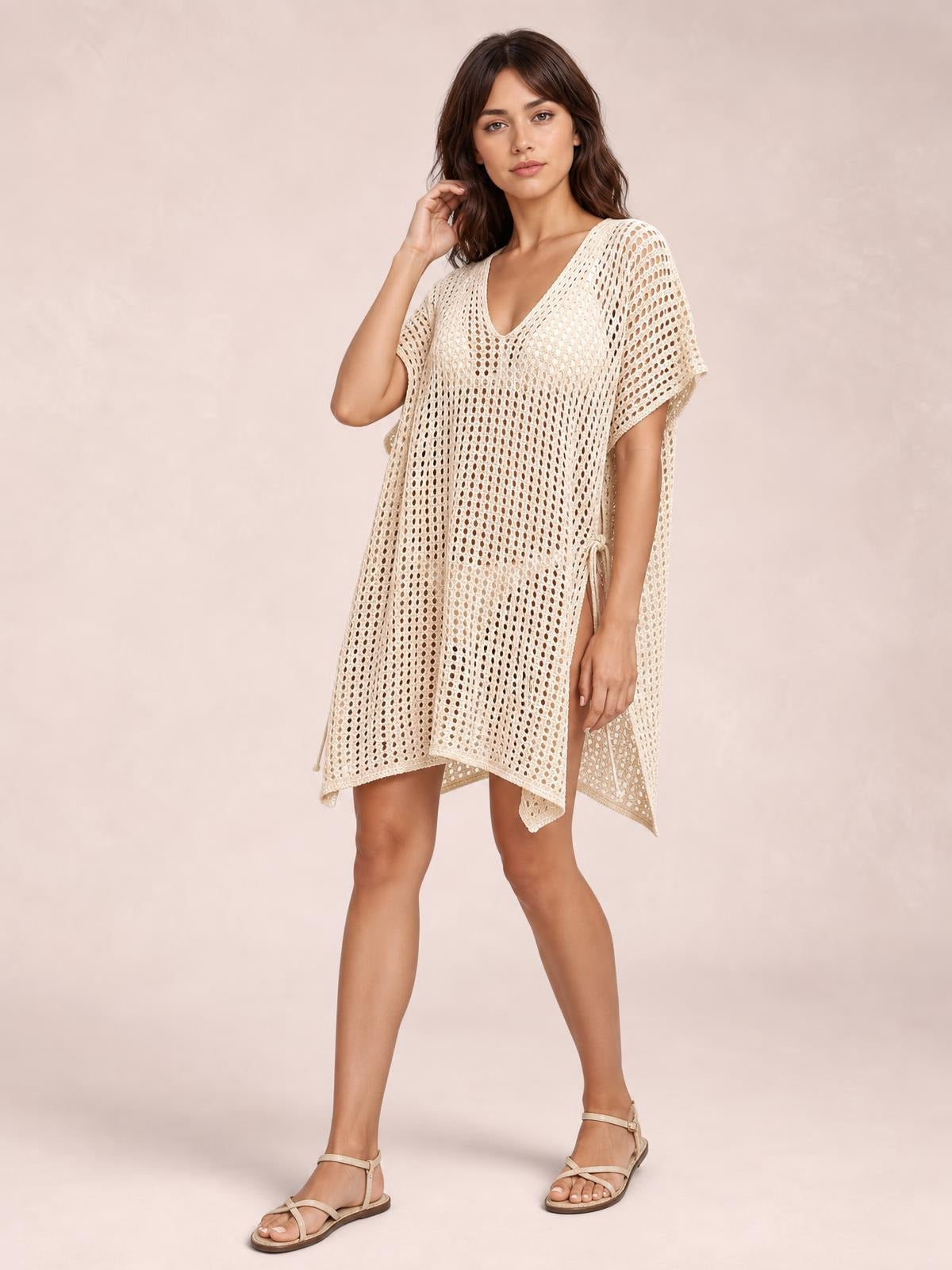 Model stands in a cream open-knit Side Tied V-Neck Cover-Up with cutout detailing, short sleeves, side ties, a loose silhouette, and an asymmetrical hem.