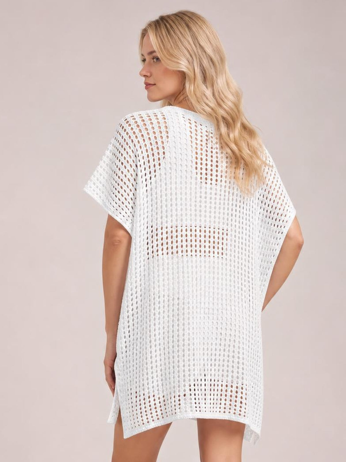 A model looks over her shoulder in a loose white open-knit cover-up with short sleeves, cutout construction, and a long relaxed silhouette.