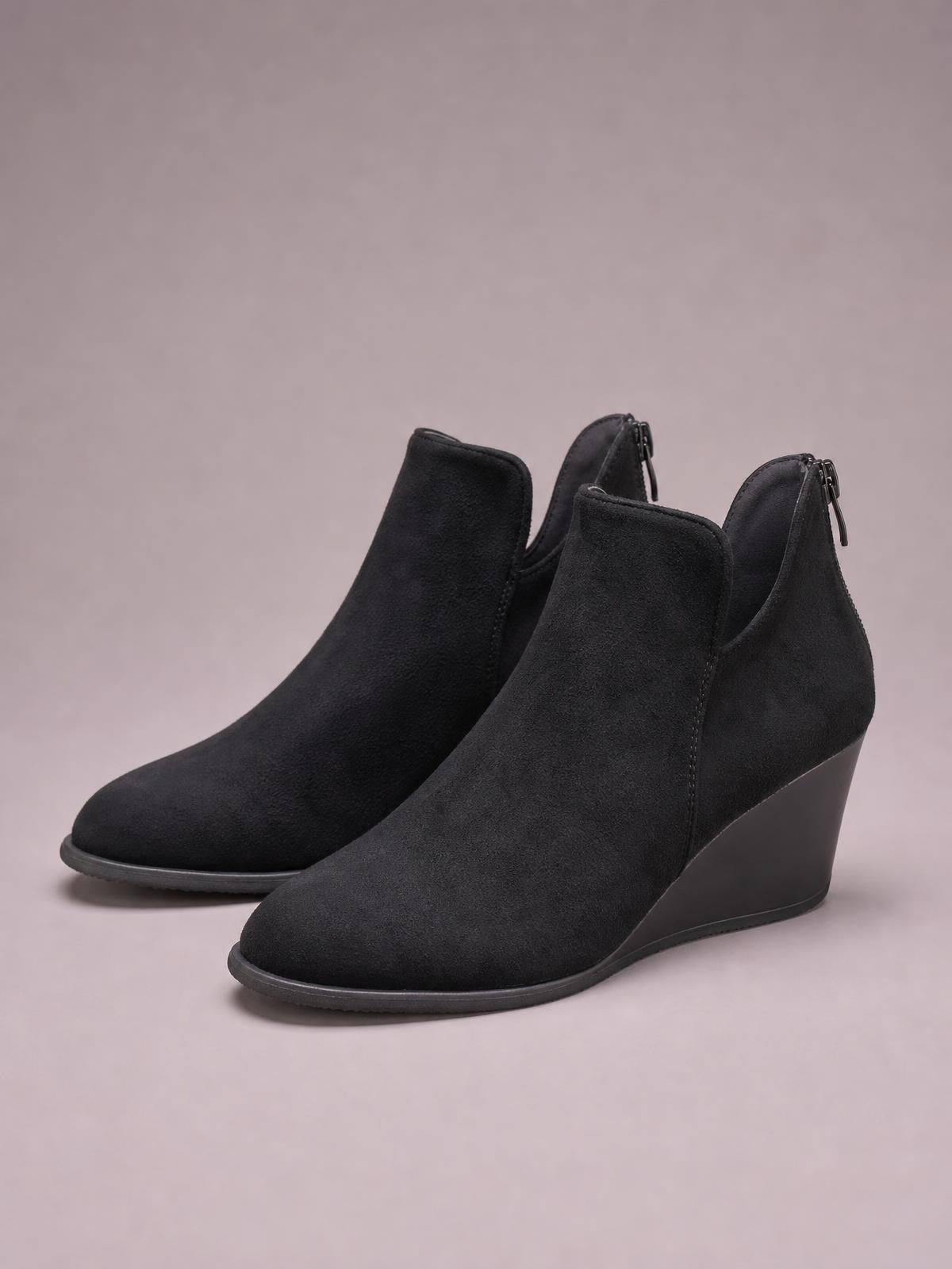 Black suede wedge boots feature rounded toes, sleek ankle-height silhouettes, side zippers, high wedge heels, and durable rubber soles.
