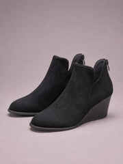 Black suede wedge boots feature rounded toes, sleek ankle-height silhouettes, side zippers, high wedge heels, and durable rubber soles.