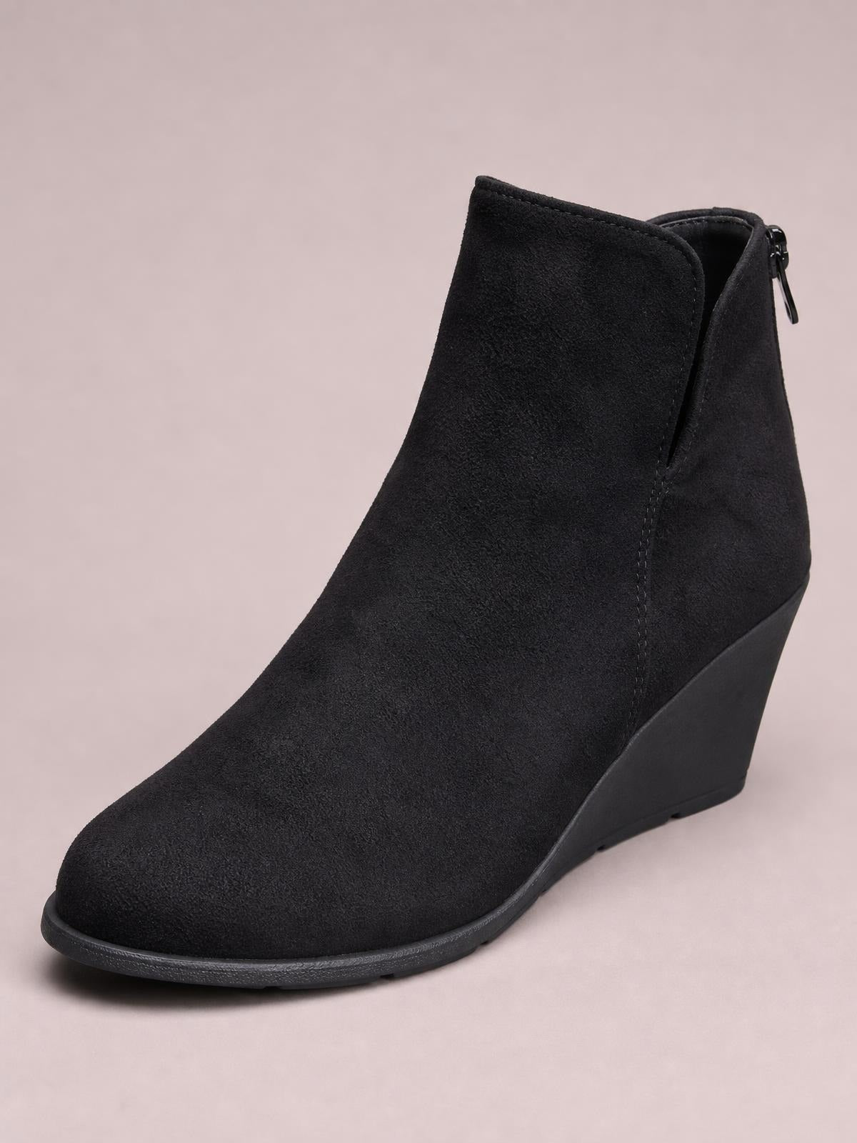 Black suede wedge ankle boot with a rounded toe, high wedge heel, clean stitched construction, and a visible side zipper with pull tab.