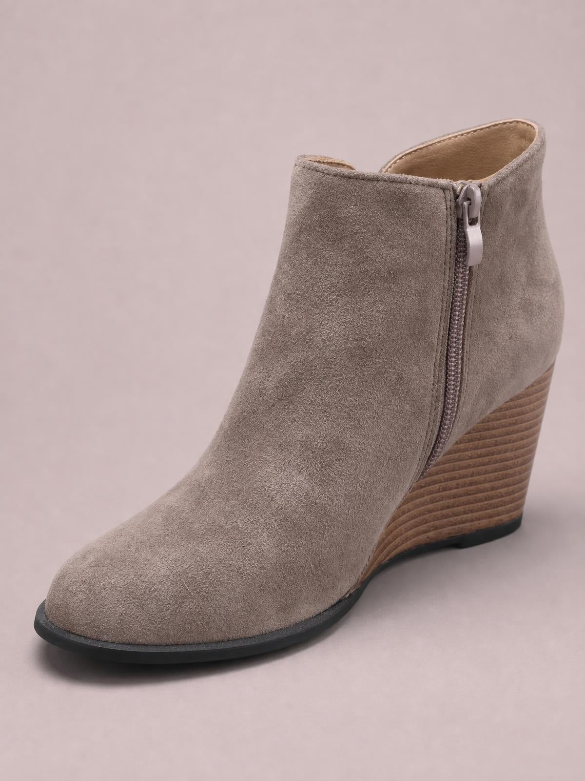 Taupe suede ankle boot with a rounded toe, visible side zipper, high wood-look wedge heel, and contrasting black rubber outsole.