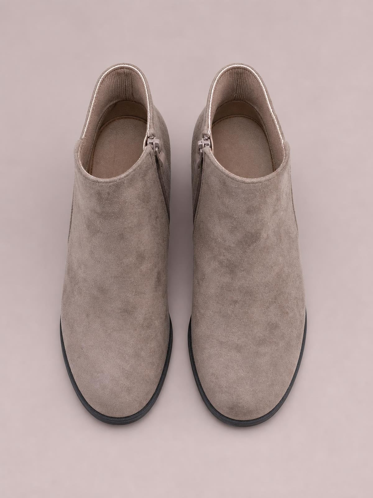 Pair of taupe suede ankle boots with rounded toes, side zippers, high wedge heels, and contrasting black rubber soles.