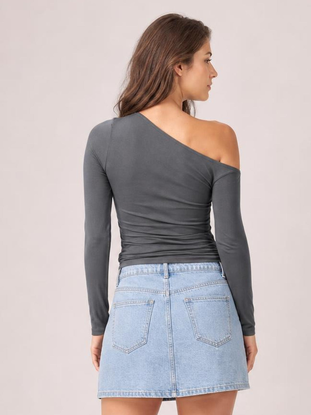 Model shown from the back in a charcoal gray single-shoulder long-sleeve T-shirt with a fitted, ruched silhouette and exposed right shoulder.