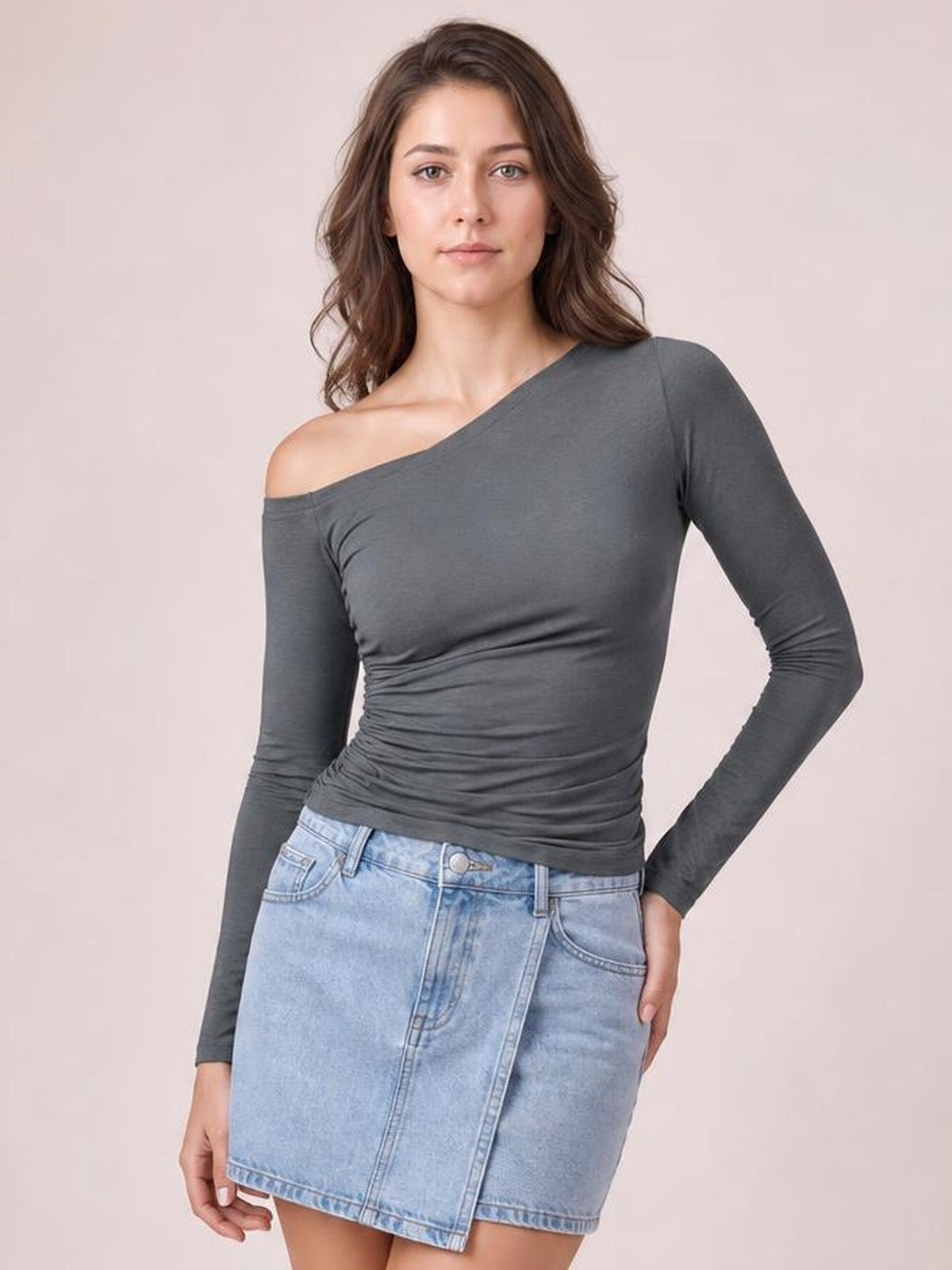 Model wearing a charcoal gray single-shoulder long-sleeve T-shirt with a fitted silhouette and ruched waist, posed with one hand on her hip.