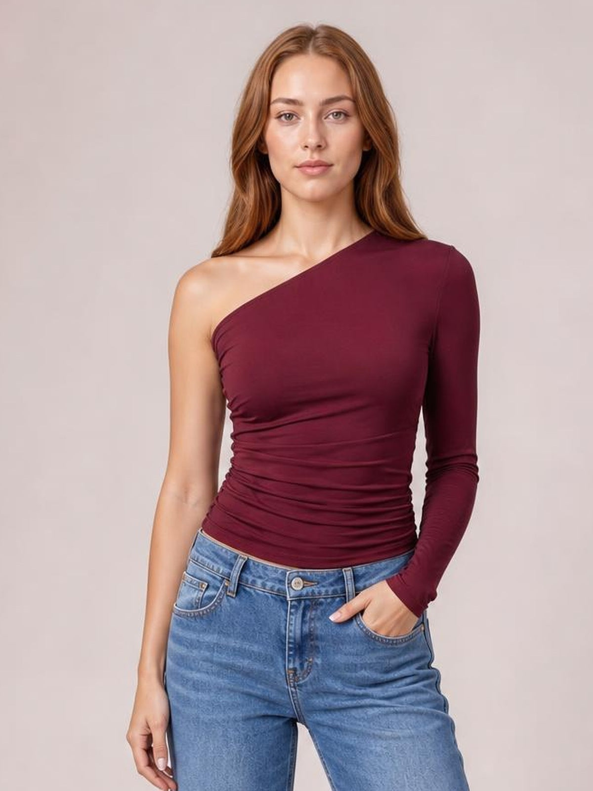 Model wearing a burgundy single-shoulder long-sleeve T-shirt with a fitted, ruched silhouette and one exposed shoulder.