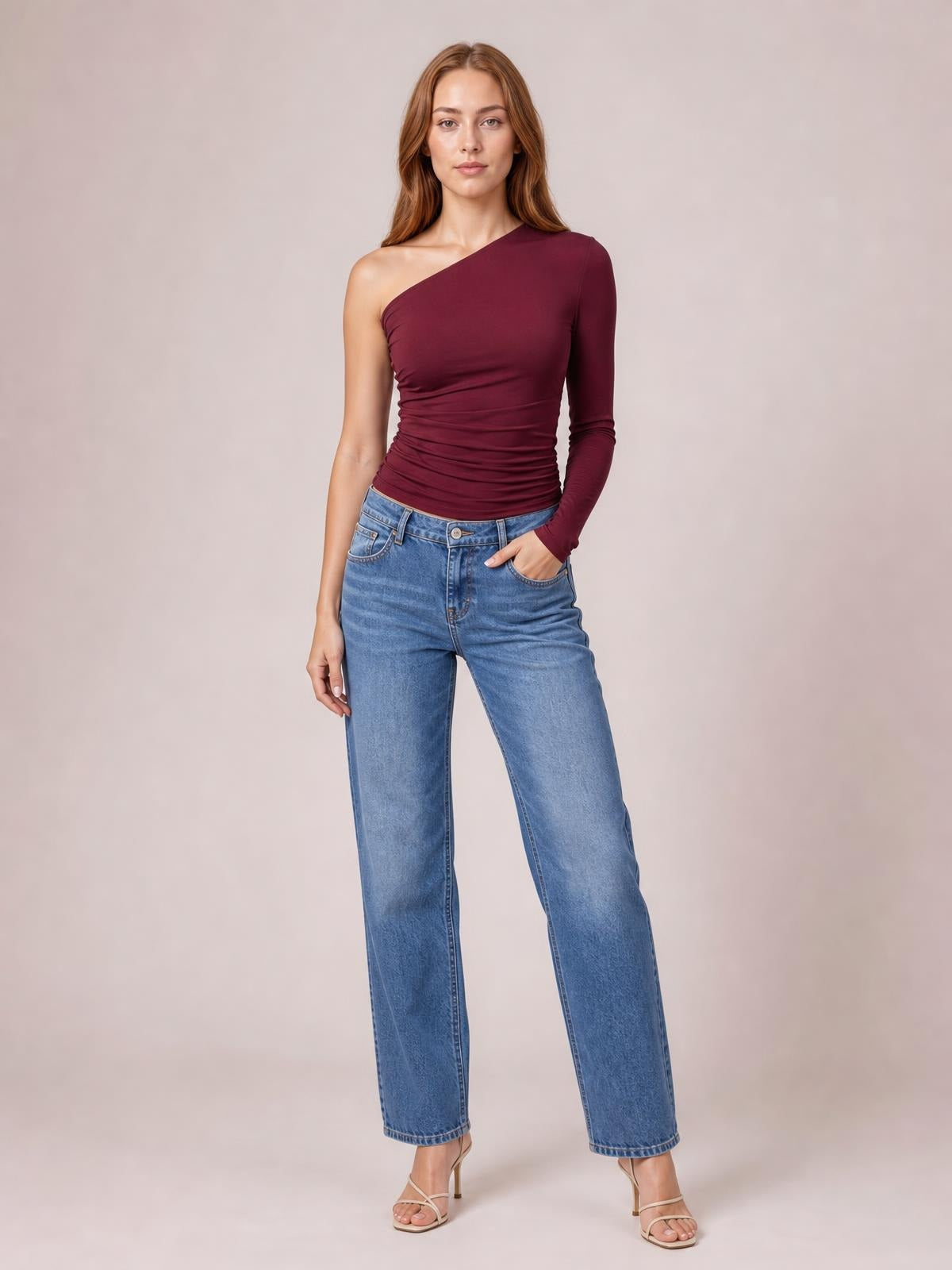 Model poses in a burgundy single-shoulder long-sleeve T-shirt with a fitted, ruched silhouette and one exposed shoulder.