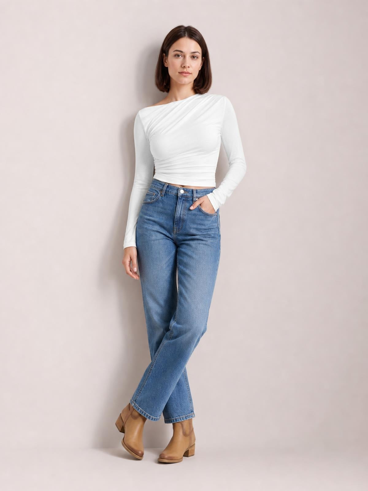 A model poses with one hand in her jeans pocket, wearing a white single-shoulder long-sleeve T-shirt with a fitted, ruched waist and asymmetric neckline.