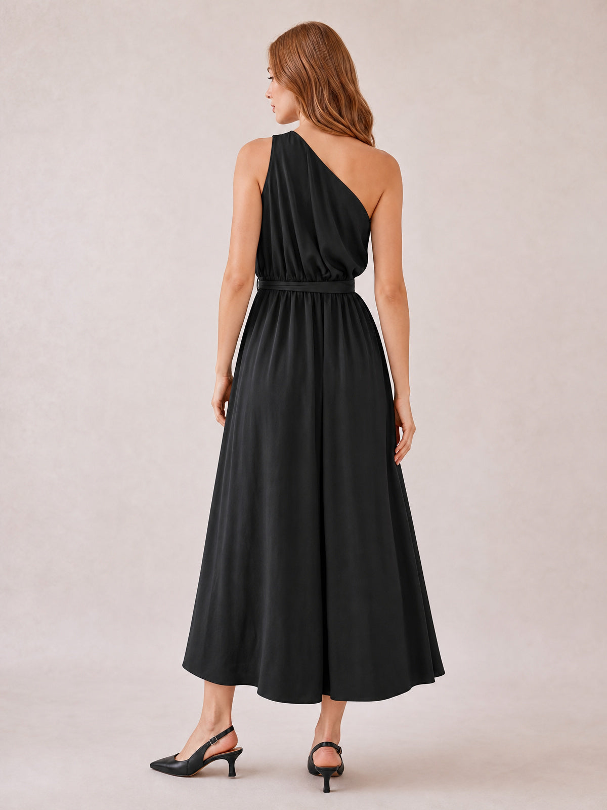 Model shown from behind in a black single shoulder midi dress with a gathered bodice, defined waist belt, and flowing A-line skirt.
