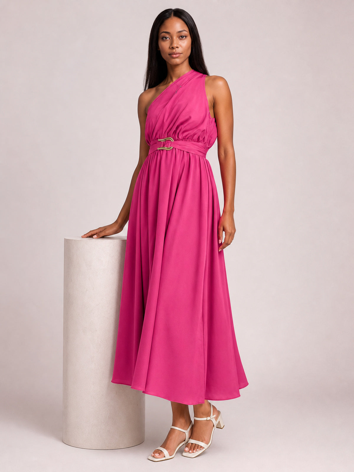 Model poses in a vibrant pink single-shoulder midi dress with a gathered bodice, defined waist, ring-detail belt, and flowing A-line skirt.
