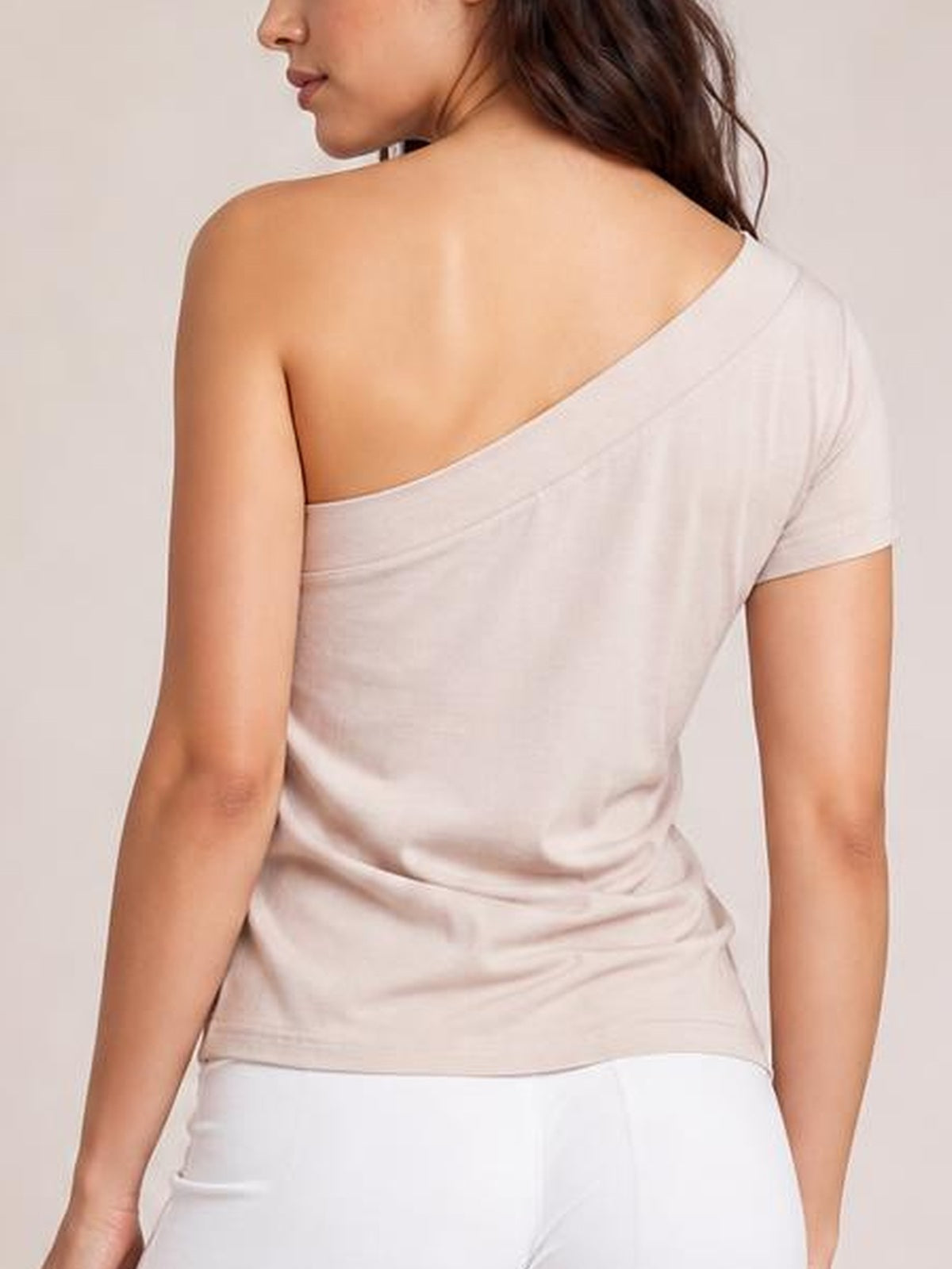 A model poses with her back turned, wearing a light pink asymmetrical single-shoulder short-sleeve top with a fitted, slightly stretchy silhouette.