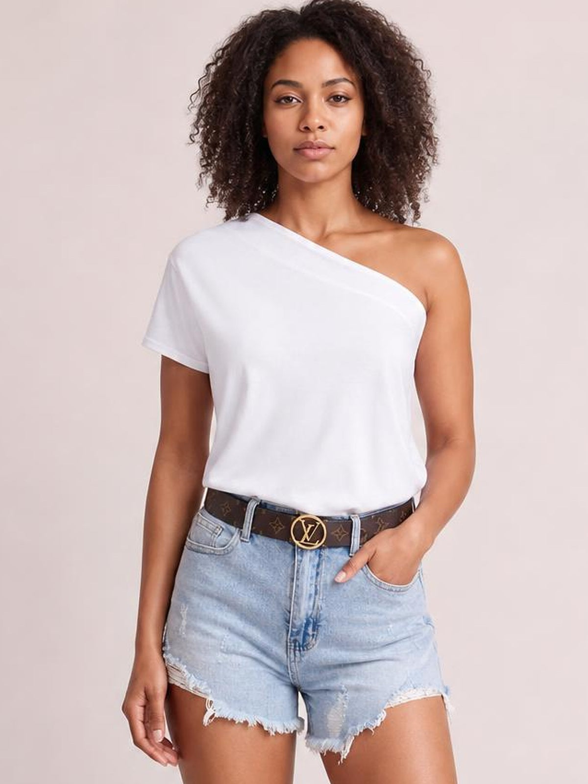 A woman poses in a white single-shoulder short-sleeve top with an asymmetrical neckline and relaxed silhouette, styled with denim shorts.