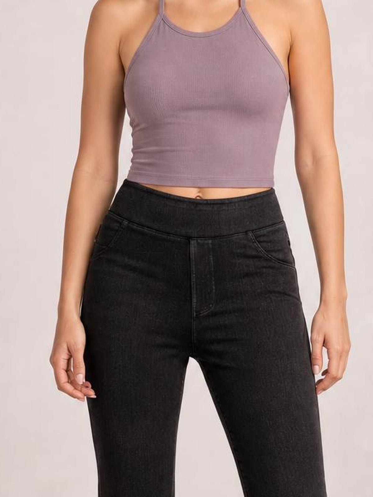Model stands facing forward in black skinny jeans with front pockets, a high-rise waistband, button closure, and a close-fitting stretch silhouette.